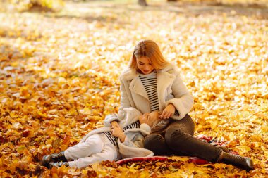Parkta neşeli bir sonbahar günü. Bir anne ve kızı, parlak sarı ağaçlarla çevrili düşmüş yapraklarda oynuyorlar. Dinlen, çocukluk, yürüyüş, aile.