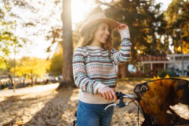 Güneşli bir sonbahar gününün tadını çıkaran bir kadın altın ormandaki yaprakların arasında bisiklet sürüyor..