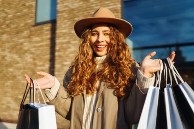 Alışveriş zamanı. Şık bir öğleden sonra gezisinde güneşli bir şehir sokağında alışveriş torbaları taşıyan genç bir kadın.