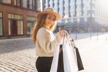 Alışveriş zamanı. Şık bir öğleden sonra gezisinde güneşli bir şehir sokağında alışveriş torbaları taşıyan genç bir kadın.