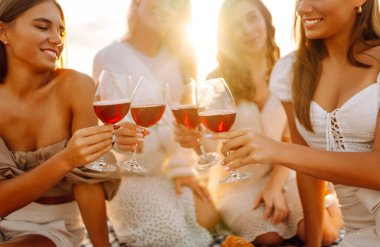 Dört arkadaş plajda kutlama yapıyor, kırmızı şarap kadehlerini kaldırıyorlar. Güneş arka planda batar, sıcak ve neşeli bir atmosfer yaratır. Kızlar partisi..