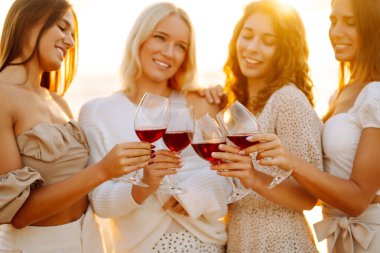 Dört arkadaş plajda kutlama yapıyor, kırmızı şarap kadehlerini kaldırıyorlar. Güneş arka planda batar, sıcak ve neşeli bir atmosfer yaratır. Kızlar partisi..