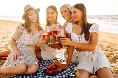 Dört arkadaş plajda kutlama yapıyor, kırmızı şarap kadehlerini kaldırıyorlar. Güneş arka planda batar, sıcak ve neşeli bir atmosfer yaratır. Kızlar partisi..