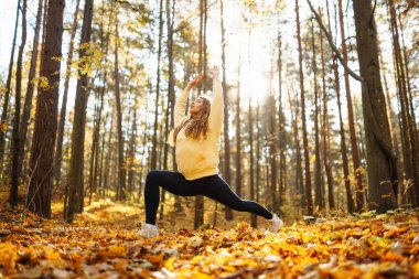 Huzurlu bir kadın, sonbahar yapraklarıyla çevrili güneşli bir ormanda yoga meditasyonu yapıyor. Yaşam tarzı ve meditasyon konsepti.