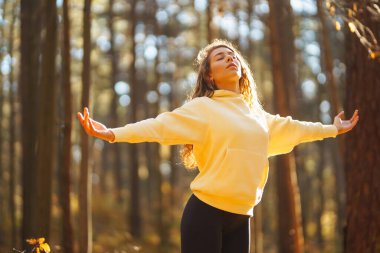 Huzurlu bir kadın, sonbahar yapraklarıyla çevrili güneşli bir ormanda yoga meditasyonu yapıyor. Yaşam tarzı ve meditasyon konsepti.