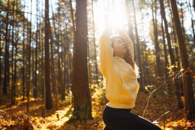 Huzurlu bir kadın, sonbahar yapraklarıyla çevrili güneşli bir ormanda yoga meditasyonu yapıyor. Yaşam tarzı ve meditasyon konsepti.