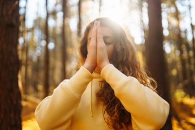 Huzurlu bir kadın, sonbahar yapraklarıyla çevrili güneşli bir ormanda yoga meditasyonu yapıyor. Yaşam tarzı ve meditasyon konsepti.