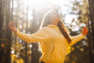 Huzurlu bir kadın, sonbahar yapraklarıyla çevrili güneşli bir ormanda yoga meditasyonu yapıyor. Yaşam tarzı ve meditasyon konsepti.