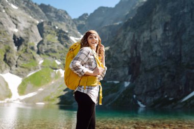 Güneşli bir doğada güneşli bir günde görkemli tepelerle çevrili çarpıcı bir dağ gölünün önünde neşeli bir yürüyüşçü gülümser. Yaşam tarzı, macera, doğa, aktif yaşam.