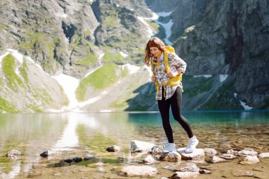 Güneşli bir doğada güneşli bir günde görkemli tepelerle çevrili çarpıcı bir dağ gölünün önünde neşeli bir yürüyüşçü gülümser. Yaşam tarzı, macera, doğa, aktif yaşam.