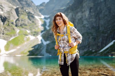 Güneşli bir doğada güneşli bir günde görkemli tepelerle çevrili çarpıcı bir dağ gölünün önünde neşeli bir yürüyüşçü gülümser. Yaşam tarzı, macera, doğa, aktif yaşam.