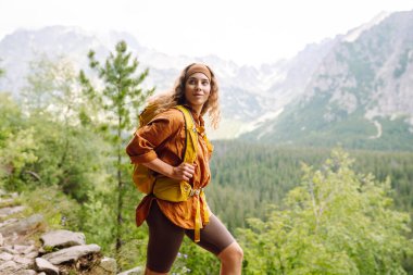 Yürüyüş yapan biri, öğleden sonra güneşinin altında yemyeşil bir arazide kayalık bir patikada yürürken temiz dağ havasının tadını çıkarır. Etkin bir yaşam biçimi kavramı.