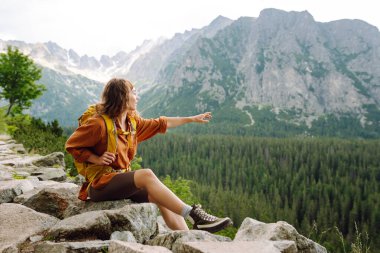 Yürüyüş yapan biri, öğleden sonra güneşinin altında yemyeşil bir arazide kayalık bir patikada yürürken temiz dağ havasının tadını çıkarır. Etkin bir yaşam biçimi kavramı.