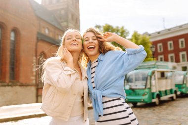 İki kadın güneşli bir şehir meydanında neşeyle kutlama yapıyor, dostluk ve mutluluk gösteriyorlar. Yaz eğlencesi konsepti. Yaşam tarzı, moda, seyahat kavramı.