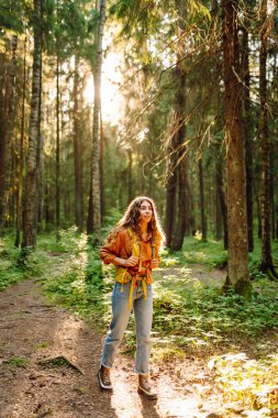 Genç bir kadın güneşli bir öğleden sonra yürüyüşü sırasında renkli yapraklarla dolu canlı bir sonbahar ormanını keşfediyor. Sonbahar manzarası.