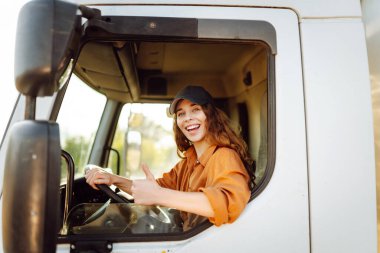 Kahverengi saçlı ve büyük bir kamyonun şoför koltuğunda otururken neşe saçan bir kadın. Halk ve endüstriyel ulaşım kavramı.