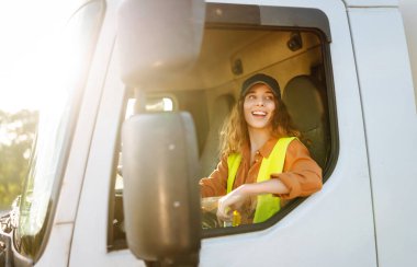 Kahverengi saçlı ve büyük bir kamyonun şoför koltuğunda otururken neşe saçan bir kadın. Halk ve endüstriyel ulaşım kavramı.