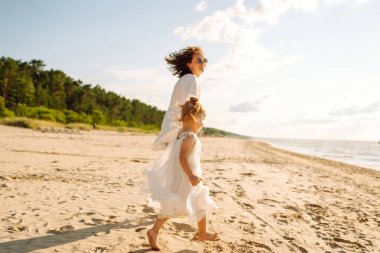 Bir anne ve kızı güneşli bir sahil gezintisinin keyfini çıkarırken, dalgalar altın saat boyunca yavaşça ayaklarına vuruyor.