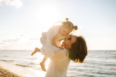 Bir anne ve kızı güneşli bir sahil gezintisinin keyfini çıkarırken, dalgalar altın saat boyunca yavaşça ayaklarına vuruyor.