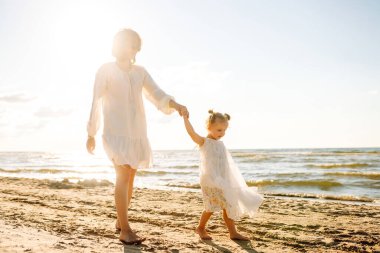 Bir anne ve kızı güneşli bir sahil gezintisinin keyfini çıkarırken, dalgalar altın saat boyunca yavaşça ayaklarına vuruyor.