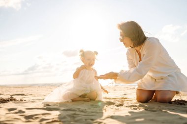 Bir anne ve kızı güneşli bir sahil gezintisinin keyfini çıkarırken, dalgalar altın saat boyunca yavaşça ayaklarına vuruyor.