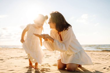 Bir anne ve kızı güneşli bir sahil gezintisinin keyfini çıkarırken, dalgalar altın saat boyunca yavaşça ayaklarına vuruyor.