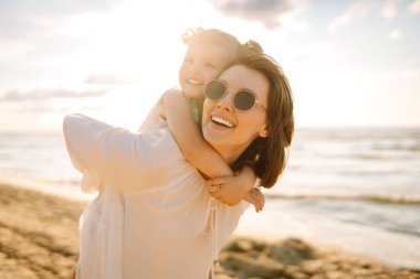 Bir anne ve kızı güneşli bir sahil gezintisinin keyfini çıkarırken, dalgalar altın saat boyunca yavaşça ayaklarına vuruyor.
