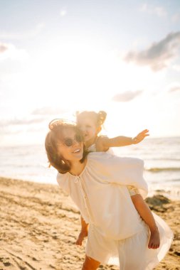 Bir anne ve kızı güneşli bir sahil gezintisinin keyfini çıkarırken, dalgalar altın saat boyunca yavaşça ayaklarına vuruyor.