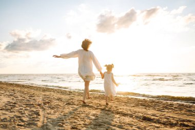 Bir anne ve kızı güneşli bir sahil gezintisinin keyfini çıkarırken, dalgalar altın saat boyunca yavaşça ayaklarına vuruyor.