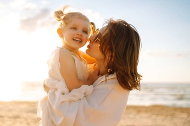 Bir anne ve kızı güneşli bir sahil gezintisinin keyfini çıkarırken, dalgalar altın saat boyunca yavaşça ayaklarına vuruyor.