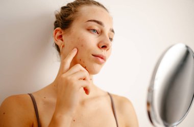 Genç bir kadın cildini doğal ışık altında inceler, cilt bakımını düşünürken lekelere odaklanır. Dermatoloji, kozmetoloji, cilt bakımı. Doğal cilt.