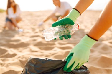 Gönüllü gruplar aktif olarak bir plaj temizliğine katılıyorlar, güzel güneşli öğleden sonranın tadını çıkarırken kumdan çöp topluyorlar, toplum ruhunu ve çevre sorumluluğunu teşvik ediyorlar. Ekolojinin korunumu kavramı.