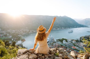 Neşeli bir kadın, Karadağ 'da güneşli bir günde dağların tepesinden Kotor Körfezi' nin çarpıcı manzarasının keyfini çıkarıyor. Avrupa seyahati. Yaşam tarzı, tatil, turizm, doğa, aktif yaşam.