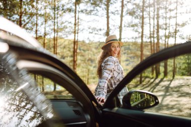 Ekose gömlekli bir kadın göl kenarında huzurlu bir gün batımının keyfini çıkarırken park halindeki arabasının yanında durmuş doğayı kutluyor. Arabayla yolculuk. Yaşam tarzı, seyahat, turizm, doğa konsepti