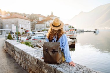 Genç bir kadın gezgin, gün batımında sakin bir sahil köyünün manzarasının keyfini çıkarıyor. Arkadan bak. Avrupa seyahati. Yaşam tarzı, tatil, turizm, doğa, aktif yaşam.