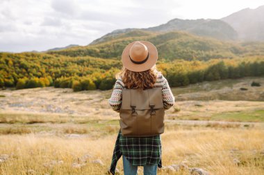 Geriye doğru bak. Seyahat eden kadın, sonbaharda kayan tepeler ve ağaçlarla dolu açık bir arazide manzaralı bir dağ manzarası keşfeder. Dağların tadını çıkarıyorum.