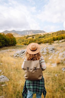 Geriye doğru bak. Seyahat eden kadın, sonbaharda kayan tepeler ve ağaçlarla dolu açık bir arazide manzaralı bir dağ manzarası keşfeder. Dağların tadını çıkarıyorum.
