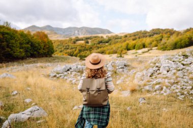 Geriye doğru bak. Seyahat eden kadın, sonbaharda kayan tepeler ve ağaçlarla dolu açık bir arazide manzaralı bir dağ manzarası keşfeder. Dağların tadını çıkarıyorum.