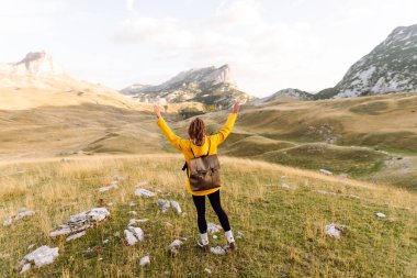 Sarı ceketli bir gezgin kadın güneşte yürüyüş yapmaktan hoşlanıyor. Sırt çantasıyla dağlarda yürüyüş. Macera aktif.