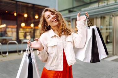 Neşeli kadın güneşli bir günde alışveriş yaparken şehir ortamında birden fazla çanta taşıyor. Tüketim, moda, alışverişler, alışveriş, yaşam tarzı konsepti.