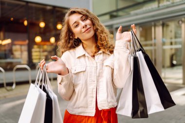 Neşeli kadın güneşli bir günde alışveriş yaparken şehir ortamında birden fazla çanta taşıyor. Tüketim, moda, alışverişler, alışveriş, yaşam tarzı konsepti.