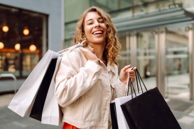 Neşeli kadın güneşli bir günde alışveriş yaparken şehir ortamında birden fazla çanta taşıyor. Tüketim, moda, alışverişler, alışveriş, yaşam tarzı konsepti.
