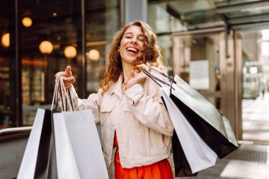 Neşeli kadın güneşli bir günde alışveriş yaparken şehir ortamında birden fazla çanta taşıyor. Tüketim, moda, alışverişler, alışveriş, yaşam tarzı konsepti.