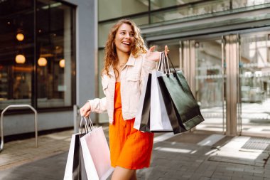 Neşeli kadın güneşli bir günde alışveriş yaparken şehir ortamında birden fazla çanta taşıyor. Tüketim, moda, alışverişler, alışveriş, yaşam tarzı konsepti.