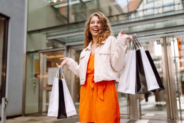 Neşeli kadın güneşli bir günde alışveriş yaparken şehir ortamında birden fazla çanta taşıyor. Tüketim, moda, alışverişler, alışveriş, yaşam tarzı konsepti.