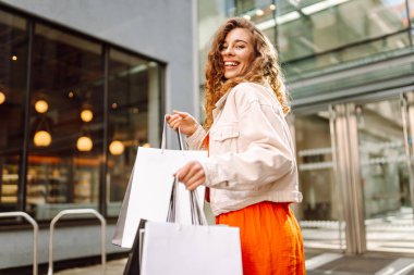 Neşeli kadın güneşli bir günde alışveriş yaparken şehir ortamında birden fazla çanta taşıyor. Tüketim, moda, alışverişler, alışveriş, yaşam tarzı konsepti.