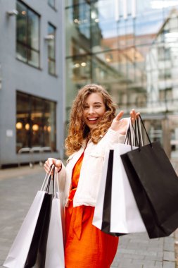 Neşeli kadın güneşli bir günde alışveriş yaparken şehir ortamında birden fazla çanta taşıyor. Tüketim, moda, alışverişler, alışveriş, yaşam tarzı konsepti.
