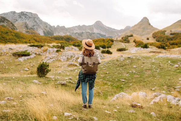 Geriye doğru bak. Seyahat eden kadın, sonbaharda kayan tepeler ve ağaçlarla dolu açık bir arazide manzaralı bir dağ manzarası keşfeder. Dağların tadını çıkarıyorum.