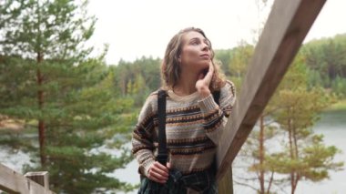 Genç bir kadın, göl kenarında huzurlu bir anın tadını çıkarırken kıtır bir sonbahar günü, doğal ortamda rahat bir kazak giyiyor.