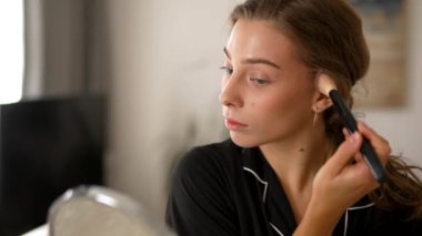 Makyaj yapan genç bir kadın, rahat bir odada oturan aynaya bakıyor. Güzel bir kadın kendini içeride güzelleştiriyor. Güzellik, makyaj konsepti.